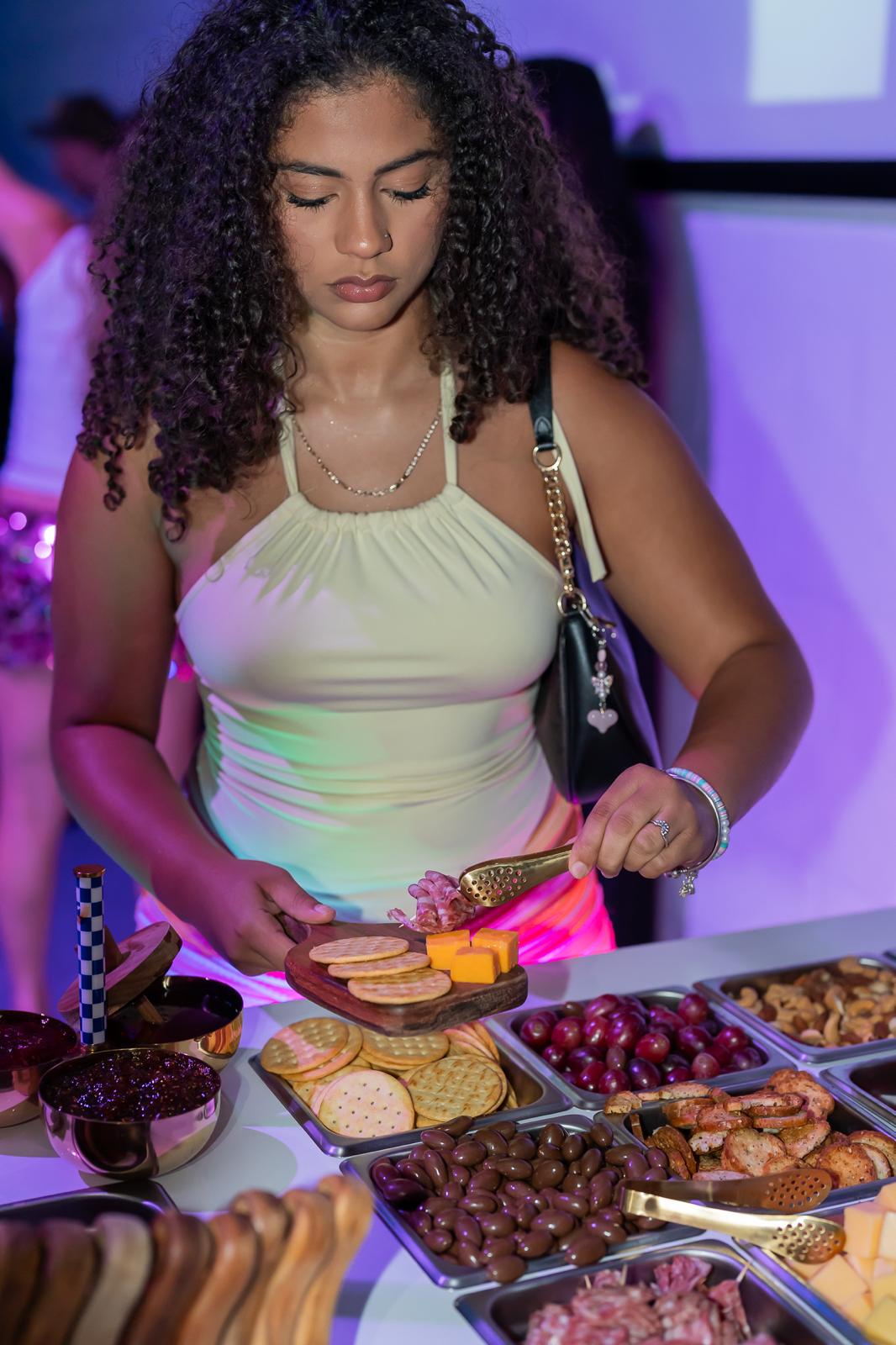 Guest using gold tongs to add salami and cheddar to her guest board at the cart
