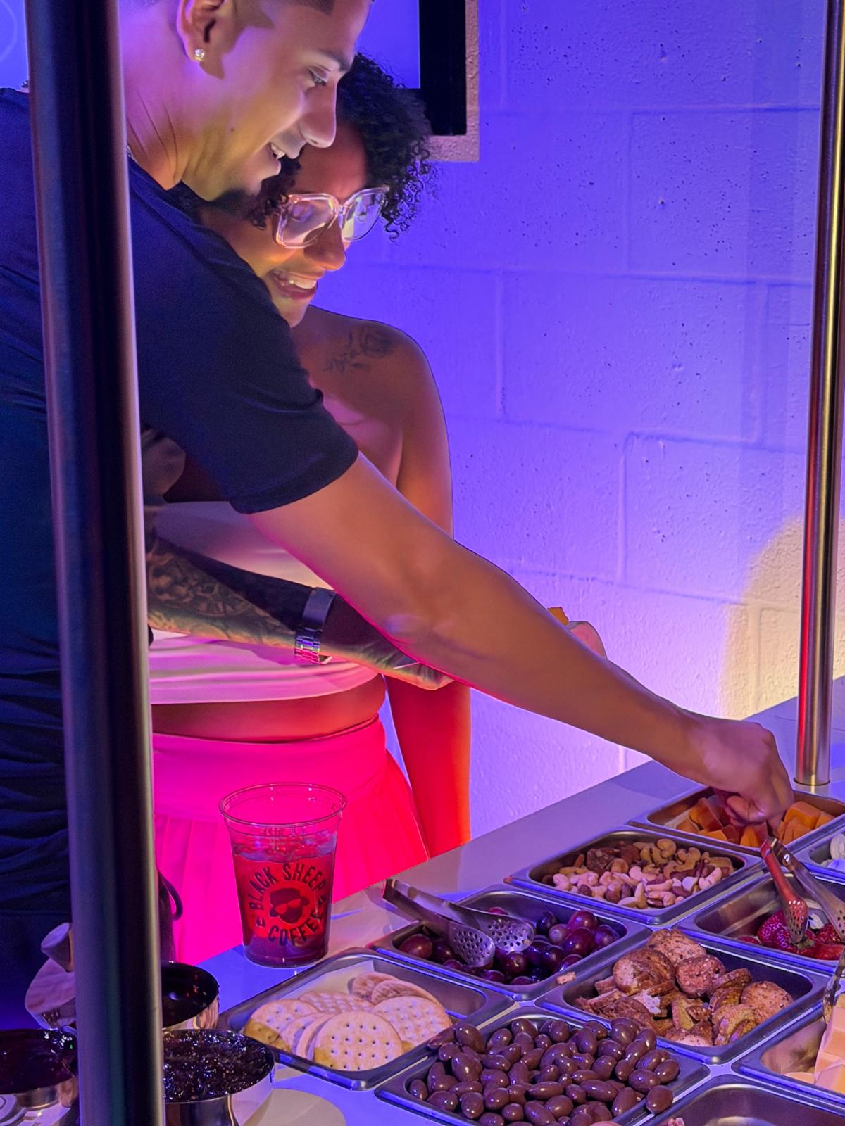 Guests reaching for cheese and fruit at the purple lit Runway Bites grazing cart